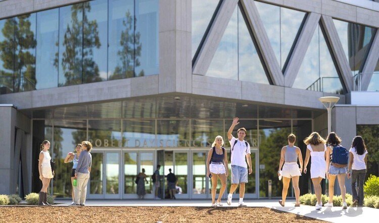 A group of students enter an angular gray building